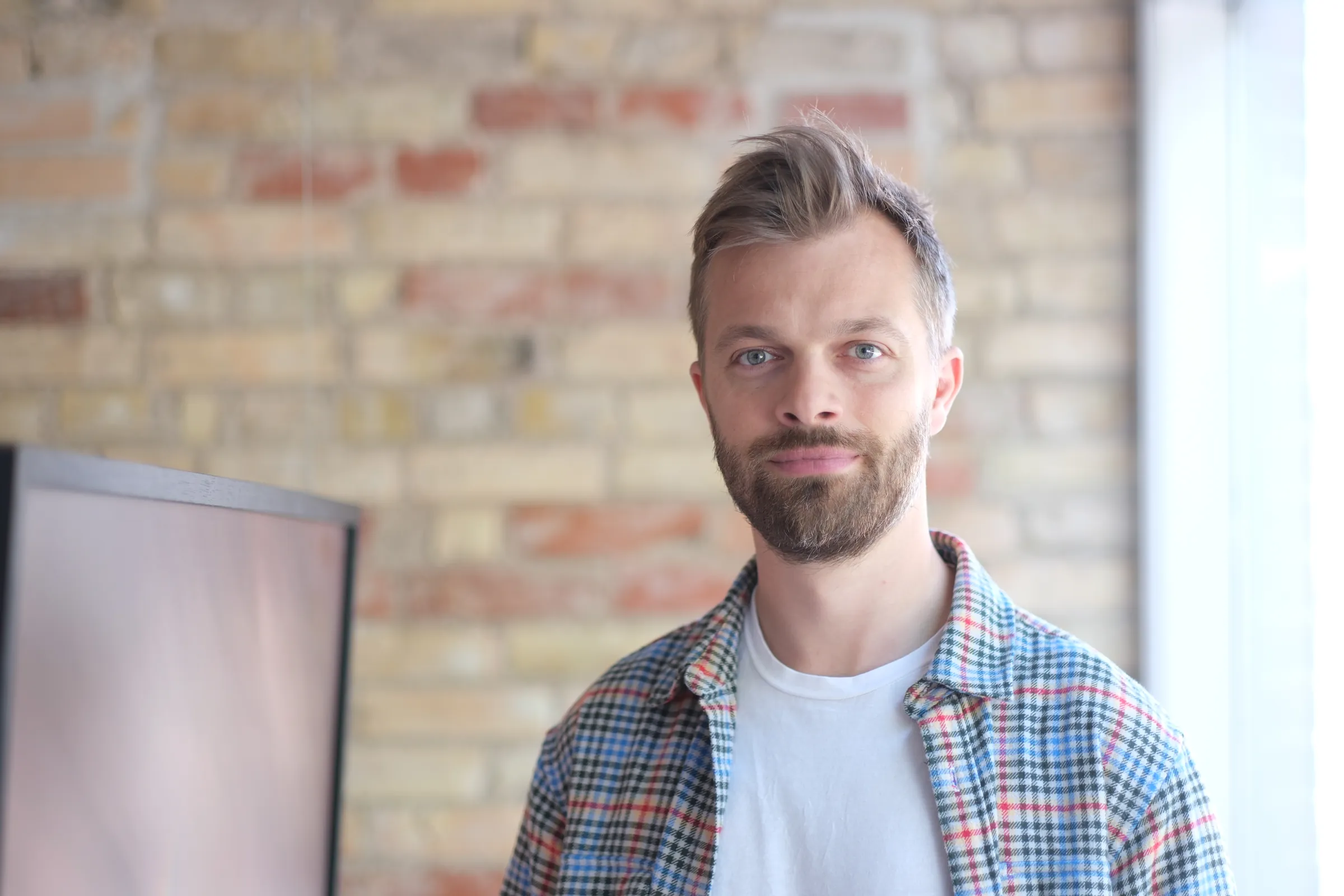 Mads Rasmussen i ternet skjorte står roligt i et lyst lokale